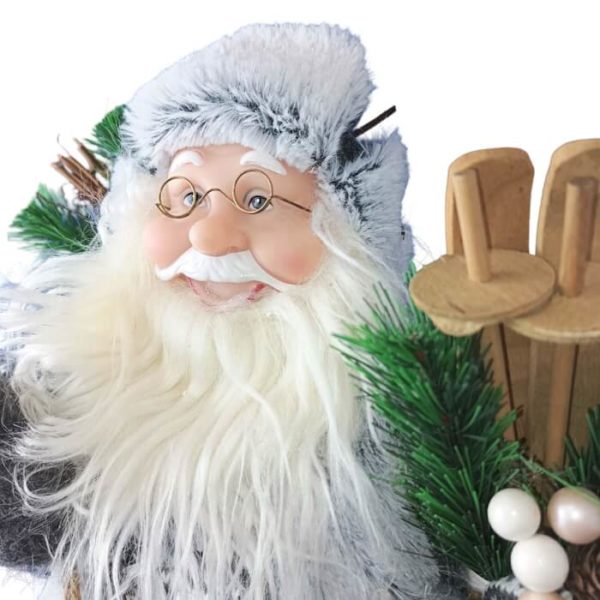 Zoom sur le Père-Noël skieur avec des skis en bois sous le bras gauche et des bâtons à droite chapka vissée sur la tête